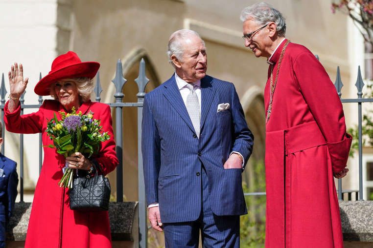 From left, Queen Camilla waves as King Charles, center, and Christopher Cocksworth speak outside