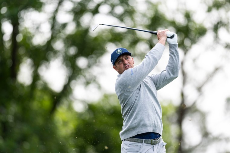 Bryson DeChambeau holds his golf club in the air after playing a stroke outside