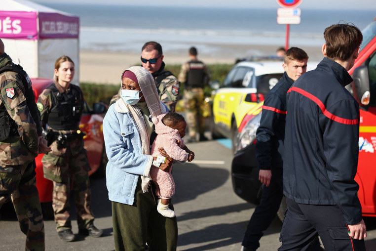 A woman with a baby stands next to rescue units after an attempt to cross the English Channel 