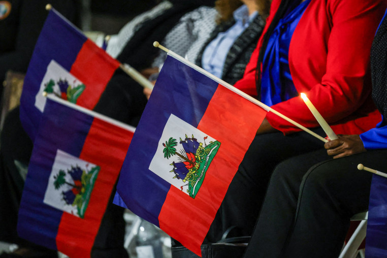 People attend a candlelight vigil and hold Haitian flags