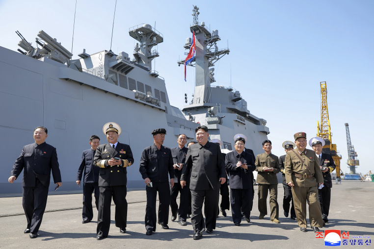 Kim Jong Un walking on a cement platform surrounded by other men in uniform.