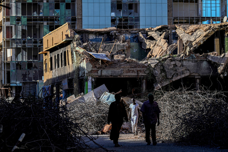 Sudanese men walk past destroyed building in the capital Khartoum.