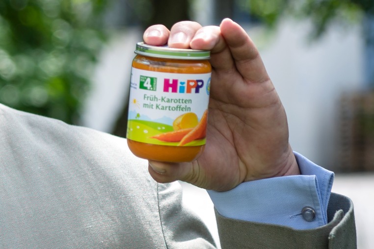 Stefan Hipp's hand holding a jar of orange baby food, carrots and a potato are seen illustrated on the food label