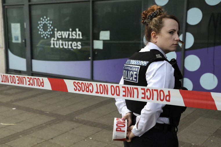 A police officer standing behind red and white striped tape glances over her right shoulder.