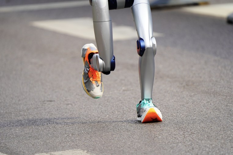 The two legs of a robot wearing running shoes are seen, from the thigh down.