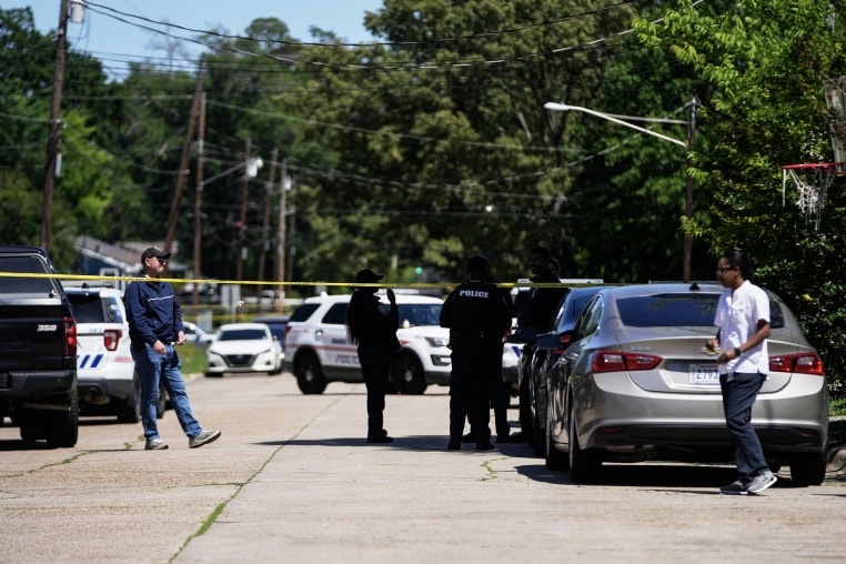 Yellow police tape stretched in front of law enforcement officials in a residential street.