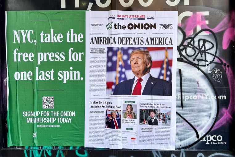 A poster for the Onion is pasted to a wall on a building, it reads "NYC, take the free press for one last spin." next to a fake newspaper article headlined "America defeats America" on top of a photo of Donald Trump