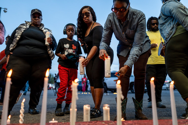 People stand in front of candles lit on the ground outside