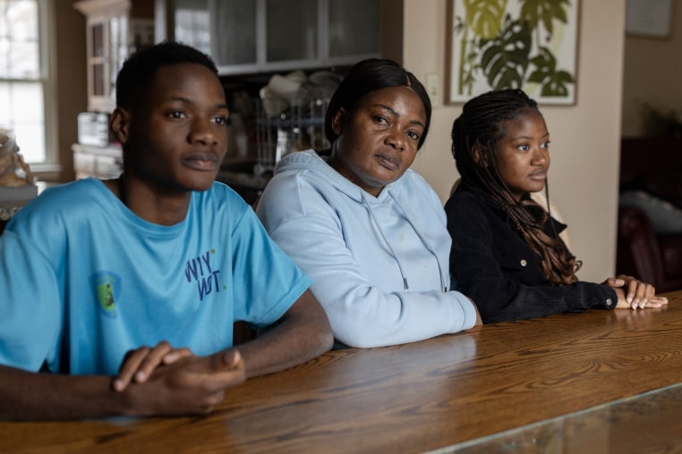 A portrait of a woman and her two teenage children seated at a wooden dining table.