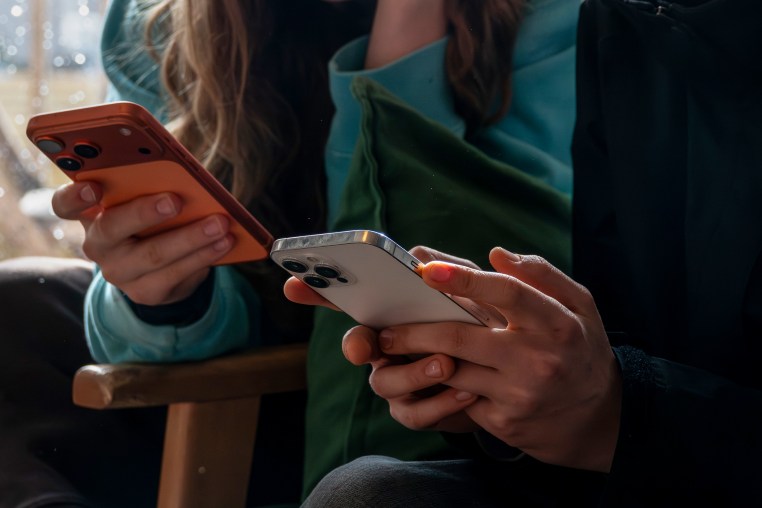 two teenagers aged 14-years-old look at their iPhone screens.
