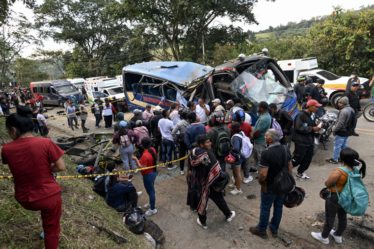 A large group of people surround a heavily damaged bus after a bombing attack on a rural highway.