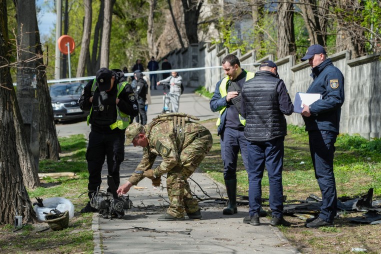 Police officers inspect fragments of a Russian drone on a sidewalk outside