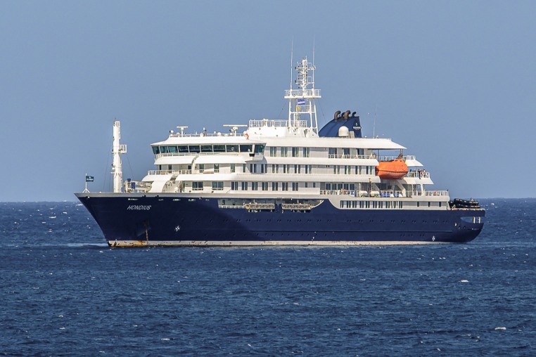 A blue and white cruise ship floats in calm waters under a clear blue sky.