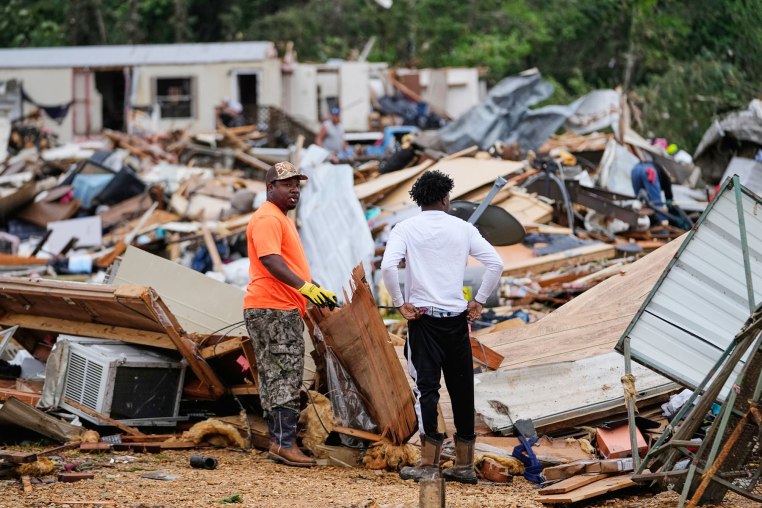 People stand among debris at Gene's Mobile Home Supply, a trailer park in Bogue Chitto, Miss., Thursday, May, 7, 2026, after a tornado cut across the state. 