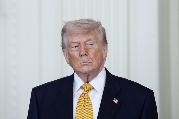 Donald Trump gazes to the side while standing in front of a white wall in the White House.