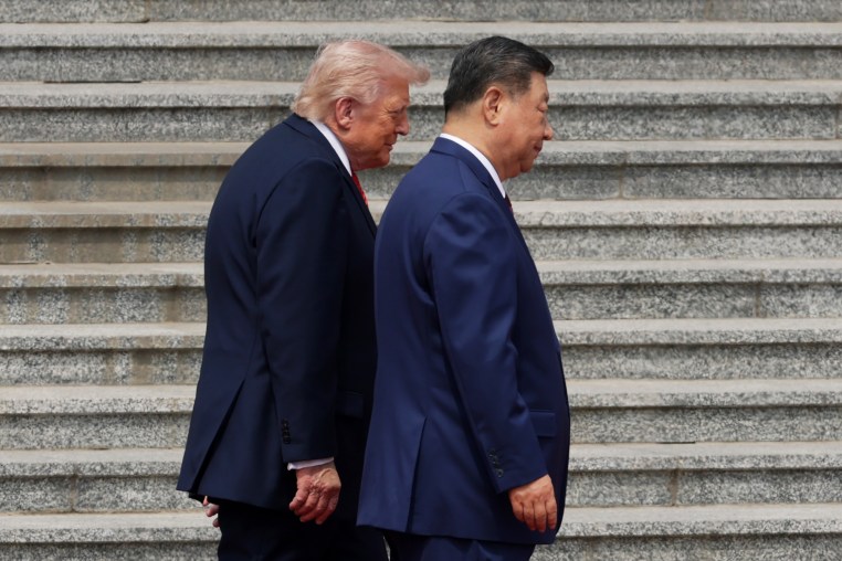 Donald Trump and Xi Jinping walk side-by-side in front of a concrete staircase.