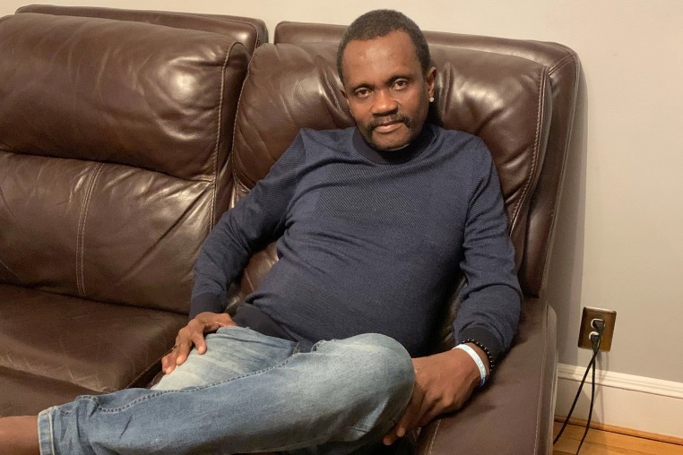 A man in a blue sweater and jeans reclined in a brown leather couch.