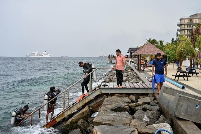 Three men wearing diving equipment make their way up a staircase from the water. 