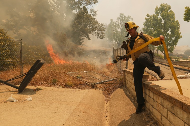 A firefighter hops over a fence while battling the Sandy Fire.