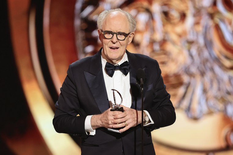 John Lithgow holding an Emmy, dressed in a tuxedo.