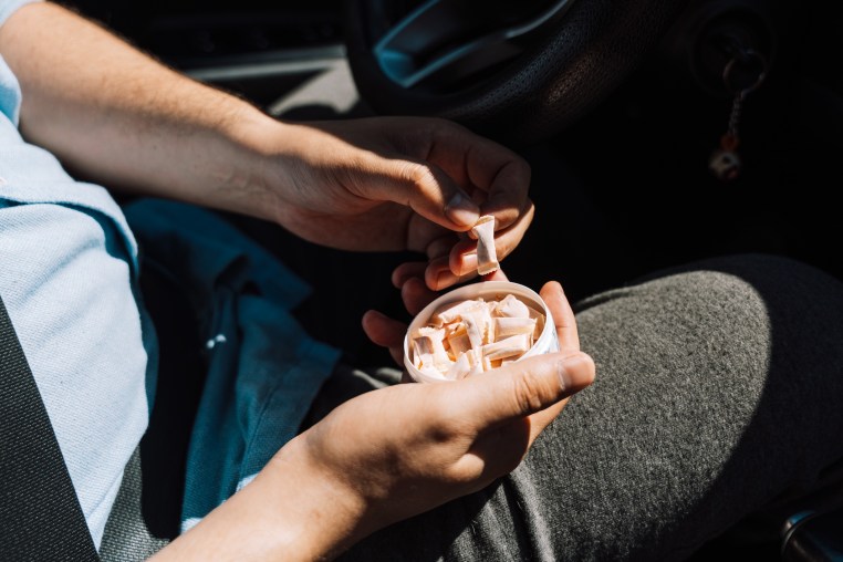 A man in a car takes out a nicotine pouch from a plastic jar