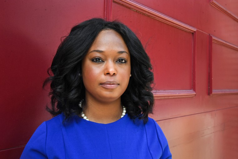 Janeese Lewis George stands for a portrait in front of a red background