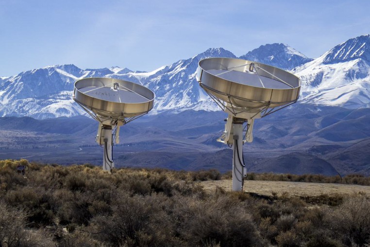 Two prototype dishes seen outside, mountainous landscape behind them