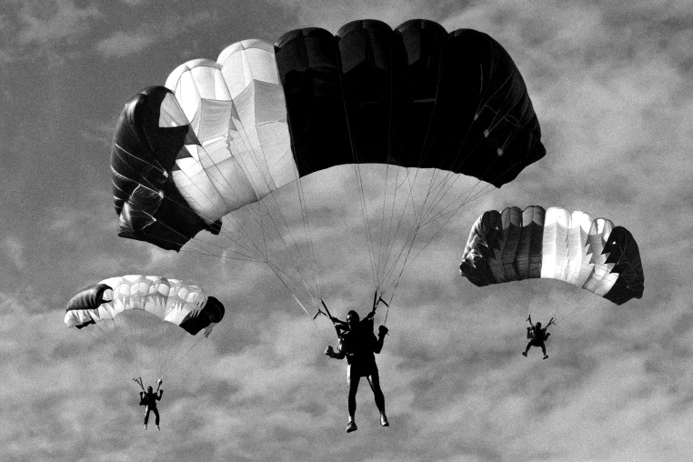 A black and white photo of three people in the sky with parachutes