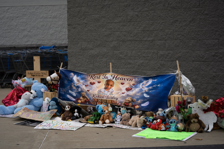 A memorial with balloons and stuffed animals in front of a Walmart.