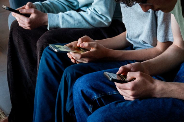Three teenagers look at their smartphone screens on April 11, 2026.