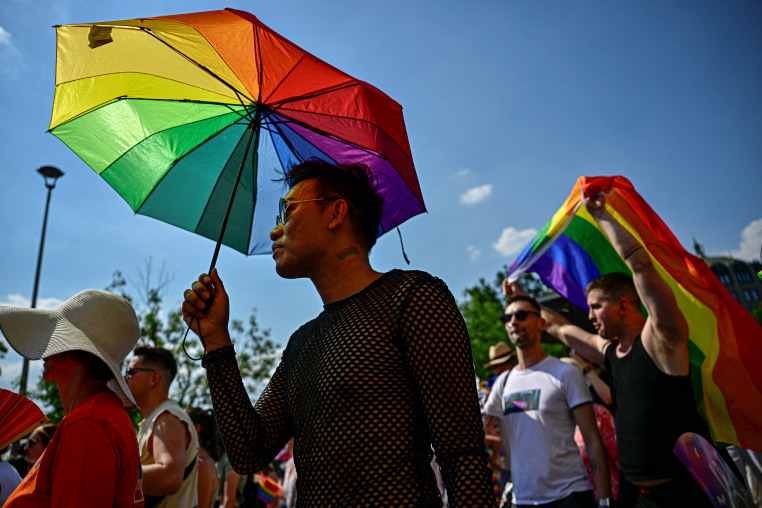 A person holds an umbrella in the colors of a Pride flag.