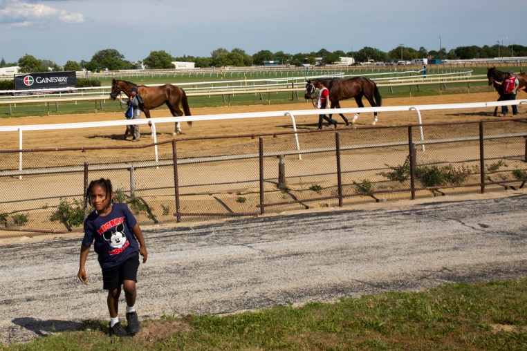 A young boy walks near a racetrack with racing horses.