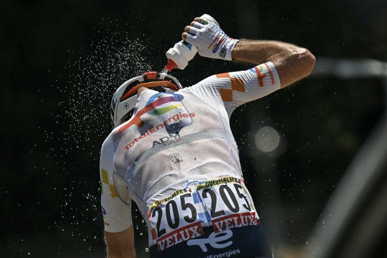 A cyclist pours a bottle of water over his back while riding.
