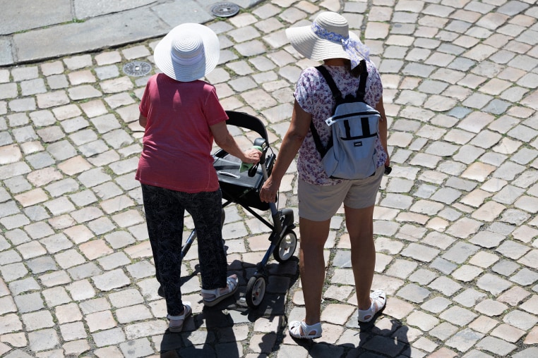 Women walking on a stone street Dresden's Old Town wearing sun hats. One woman has a walker.