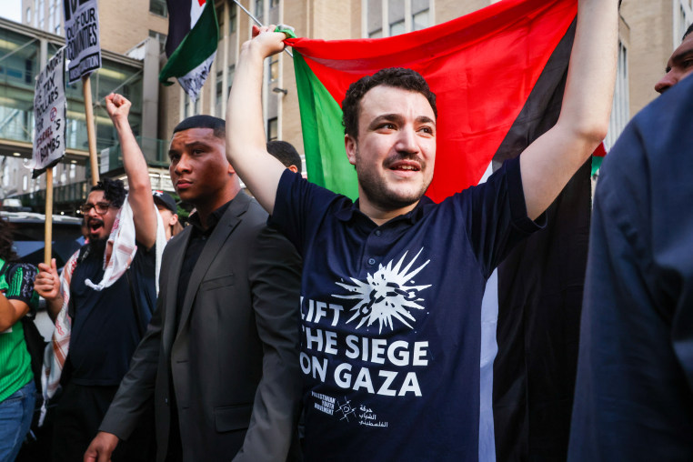 Mahmoud Khalil hold a Palestinian flag behind his back and wears a black shirt with white text on the front that reads "Lift the siege on Gaza"