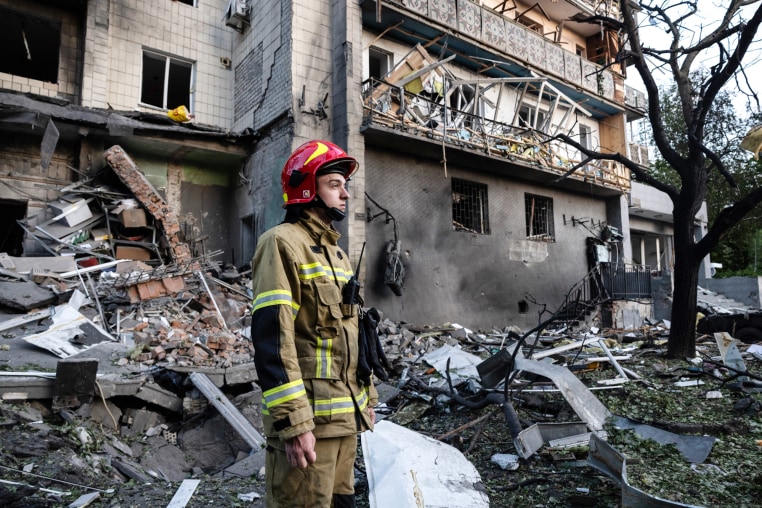 A firefighter stands near a destroyed building with rubble
