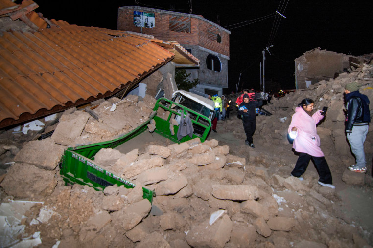 People walk amid debris outside near houses, photo taken with flash at night