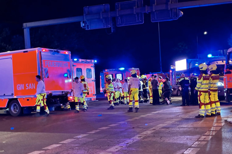 Emergency workers in fluorescent safety gear in front of ambulances at night.