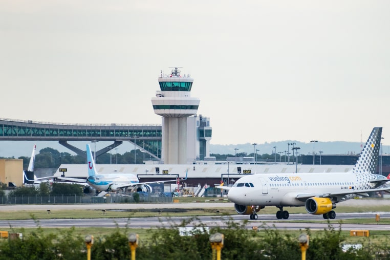 Image: A Vueling Airlines S.A. Airbus A319-100 turns off the runway in front of the air traffic control tower and the Gatwick Pier 6 Bridge