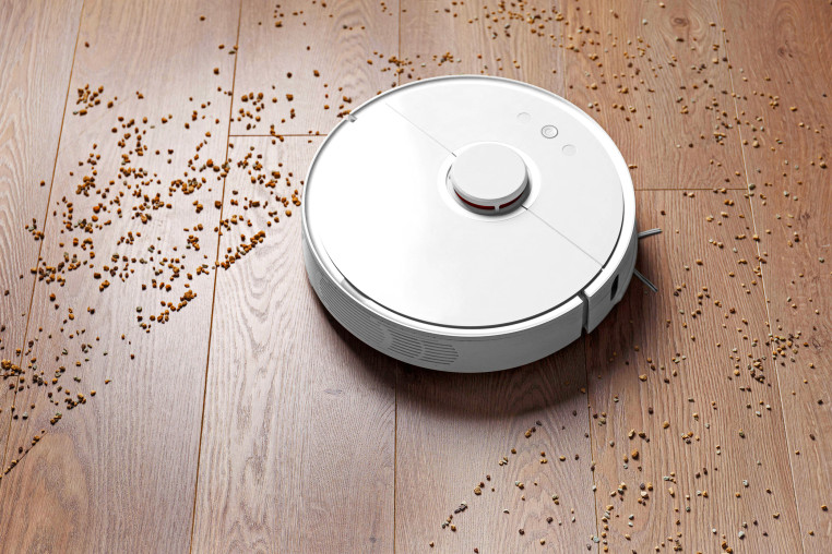 Image: Smart robot vacuum cleaner removes scattered debris from the laminate floor. The concept of a smart home, wireless cleaning of any surfaces