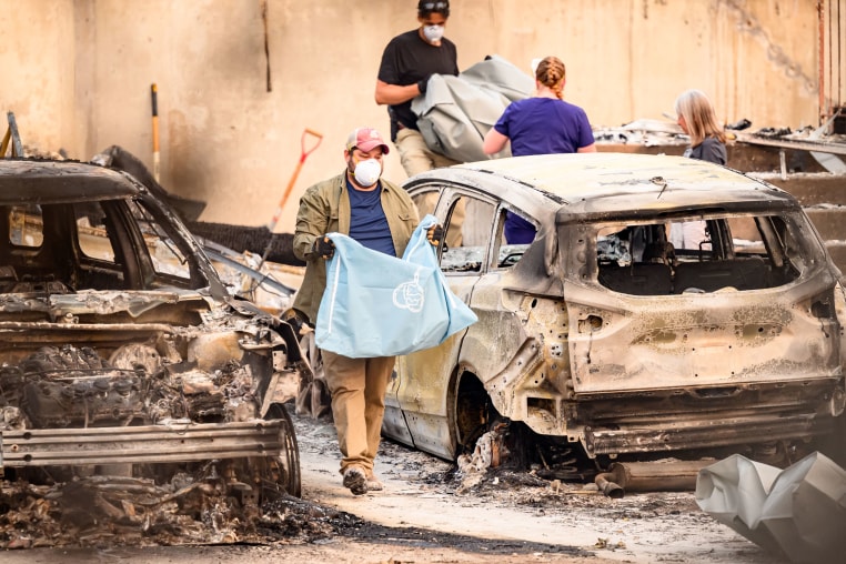 Residents carry the remains of deceased dogs at a home burned in the Old Trails fire in Spokane, Wash., on Aug. 4, 2026.