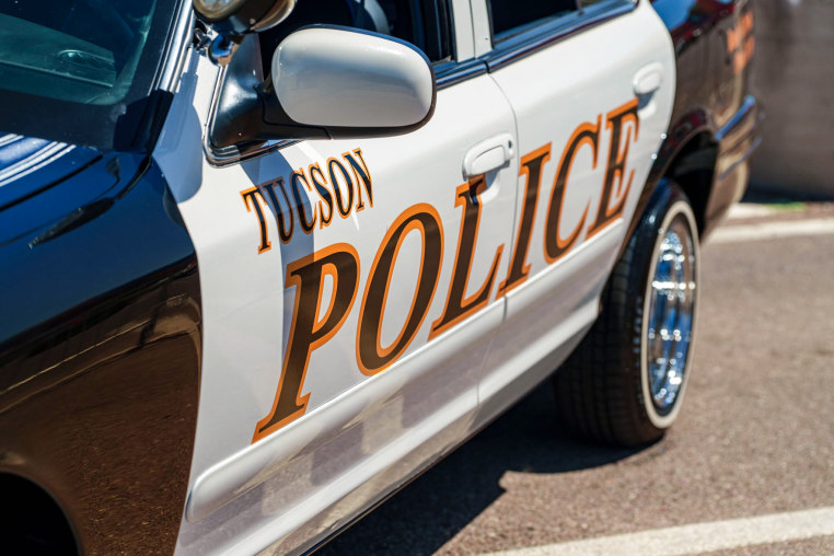 The side doors of a Tucson Police department vehicle (sedan style), with Tucson Police in black text with yellow text overlay on top of the two white side doors