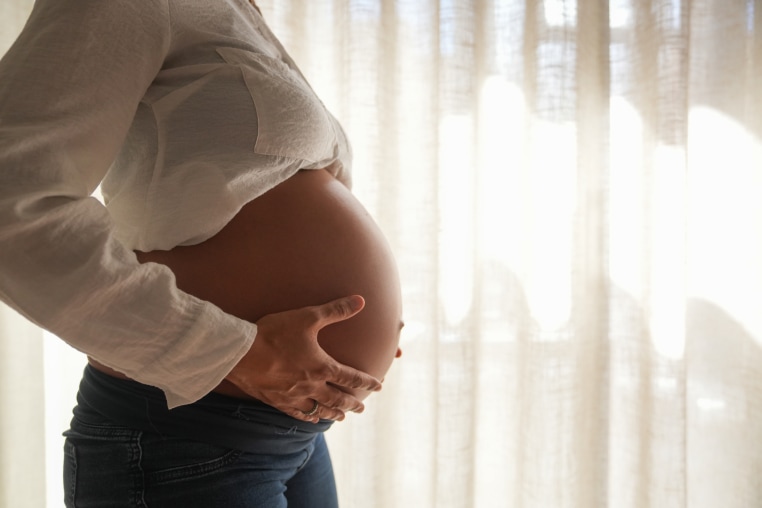 A pregnant woman holds her belly with her two hands.