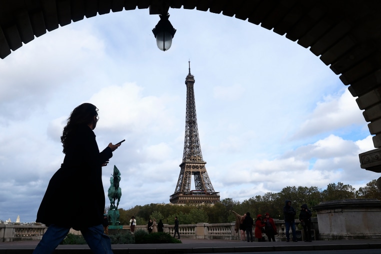 A woman checks her phone as she walks on a bridge, Thursday, Nov. 2, 2023 in Paris. (AP Photo/Aurelien Morissard)