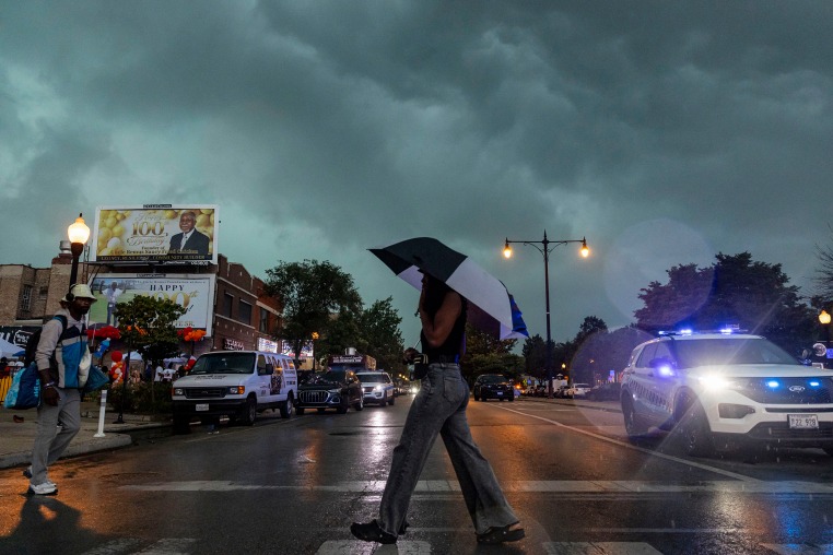 A woman crosses the street while holding an umbrella as a rain storm appears to occur. 