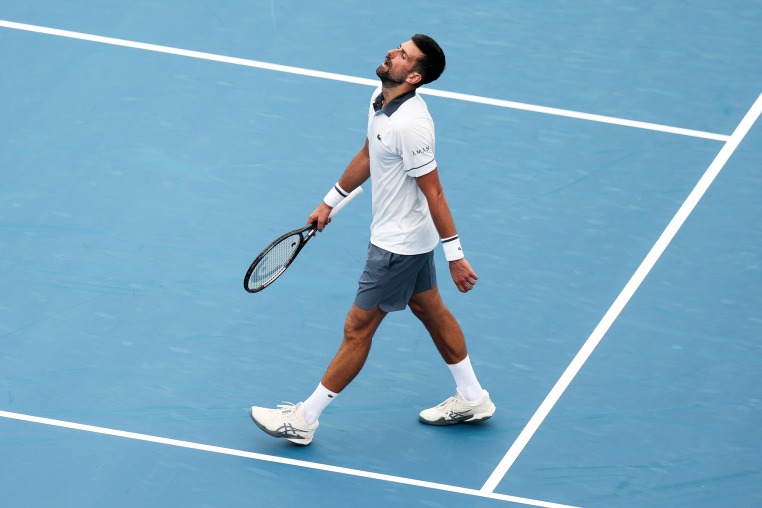 Novak Djokovic walks on the tennis court holding his racket while tilting his head back