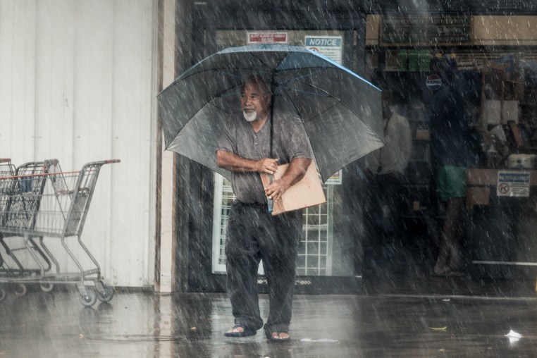 A man with a large umbrella stands in a downpour.