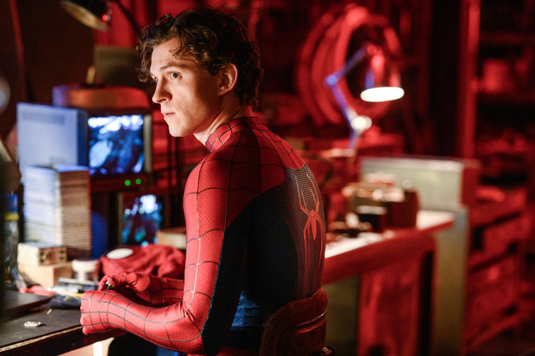 Tom Holland wearing a Spider Man suit and sitting at a work desk