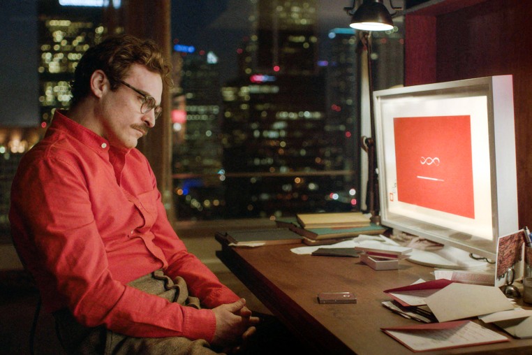 Joaquin Phoenix sits at a computer desk and looks at a loading screen on a computer screen