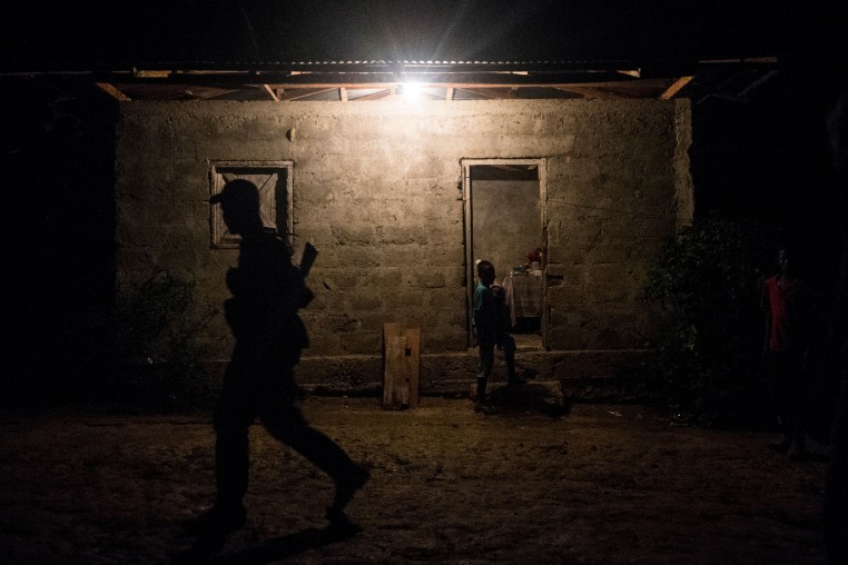 A guerrilla member walks in front of a house as a child appears to walk-in.